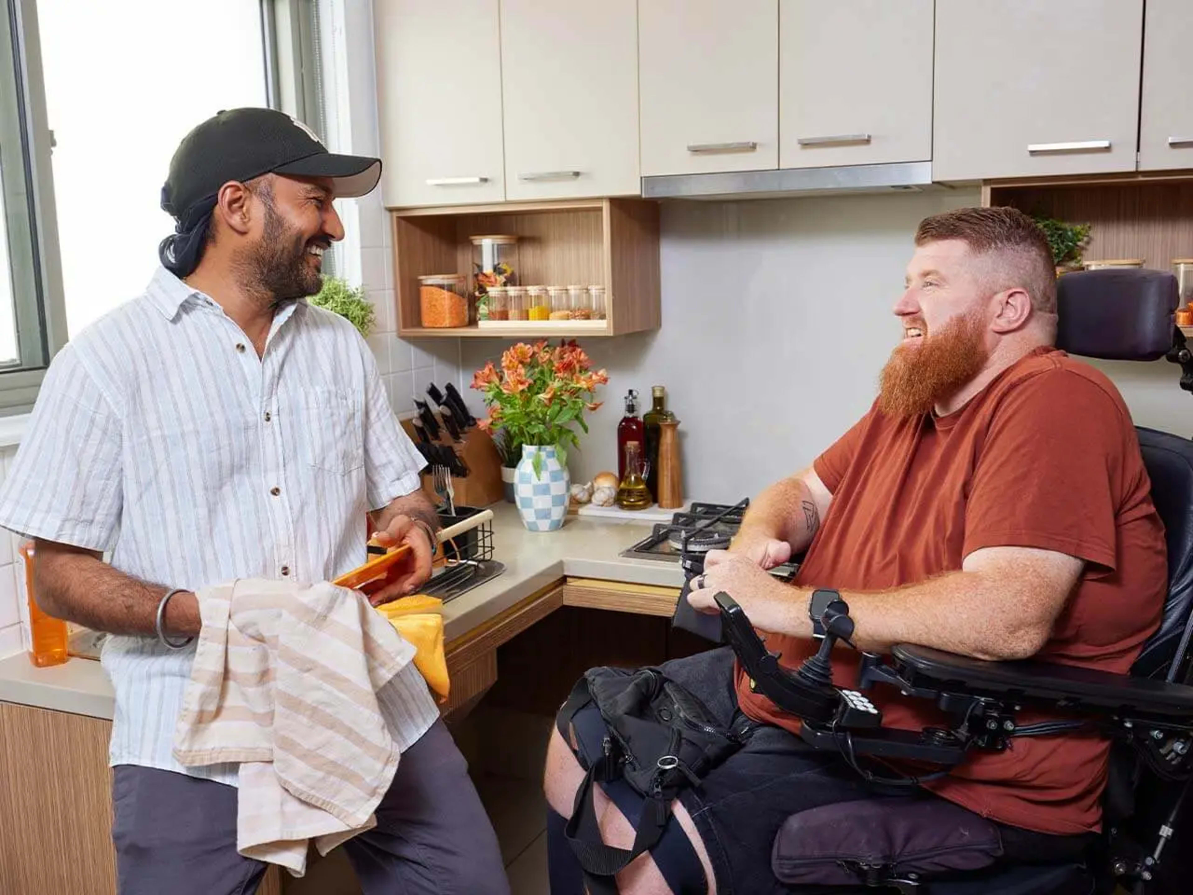 Support worker dries dishes while talking to a client in a wheelchair.