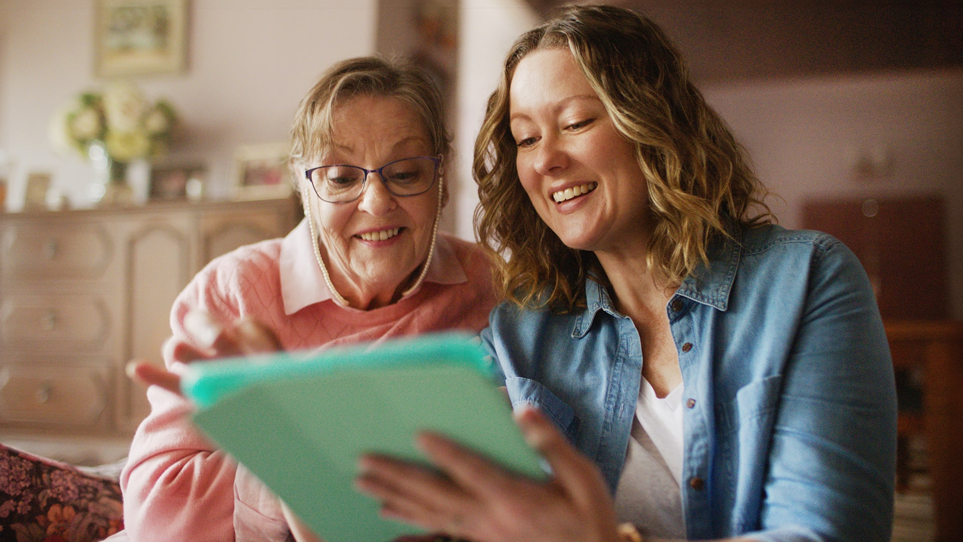 A younger woman and an older woman look at a tablet together.