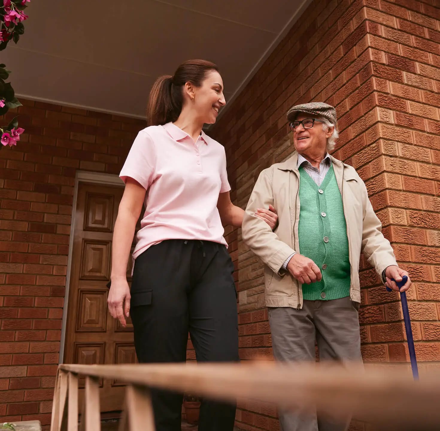 A support worker helps her older client as they leave the house together.
