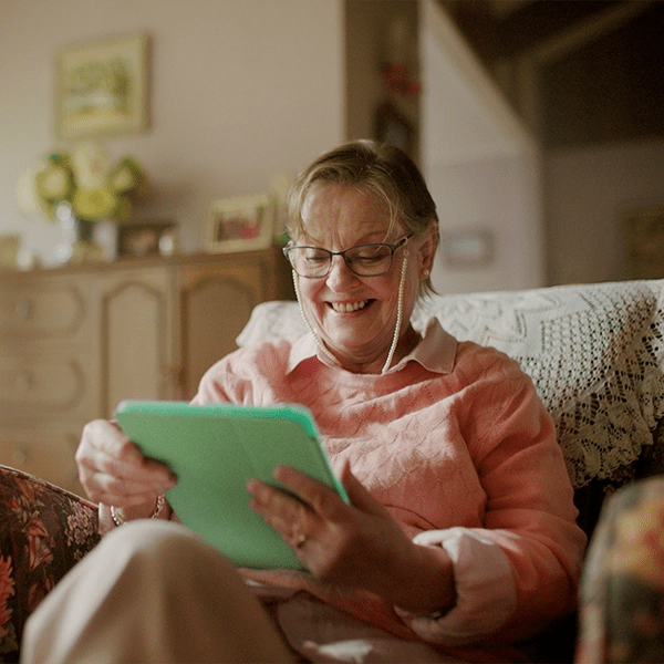 An older woman sits in a chair using her tablet.