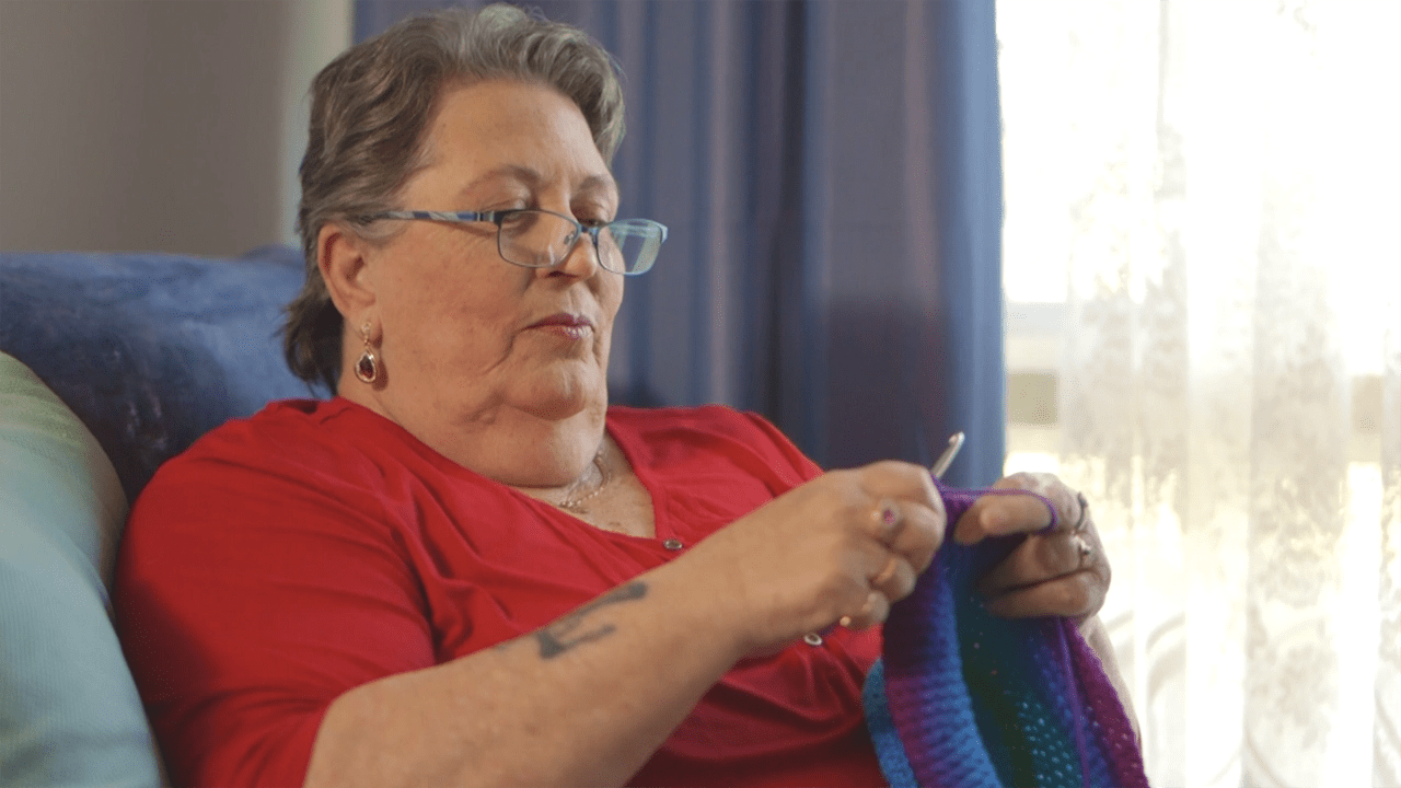 Christine sits in a chair, knitting.