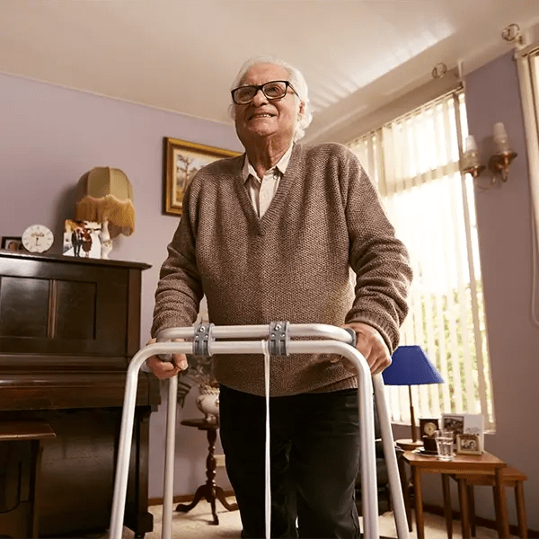An older man using his walking frame in his living room.