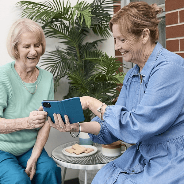 A support worker and her older client look at a smartphone together.